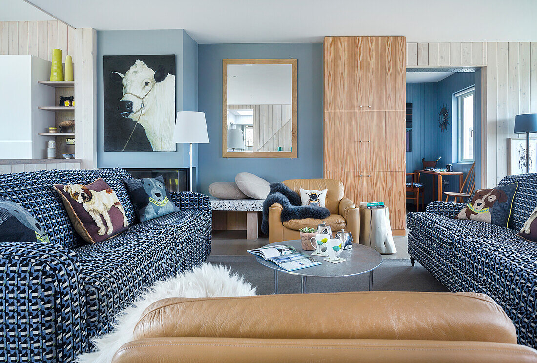 Open plan living room with blue and white covered sofas and light brown leather armchairs