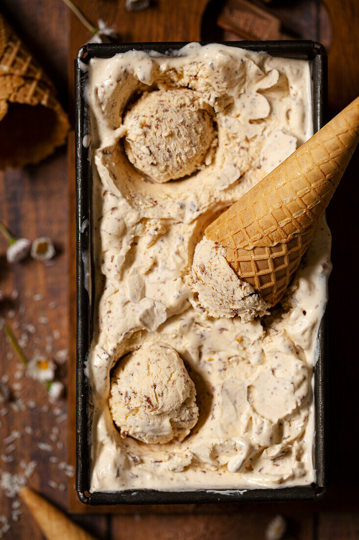 A tub of coconut ice cream with balls scooped out and a waffle cone restinbg on top