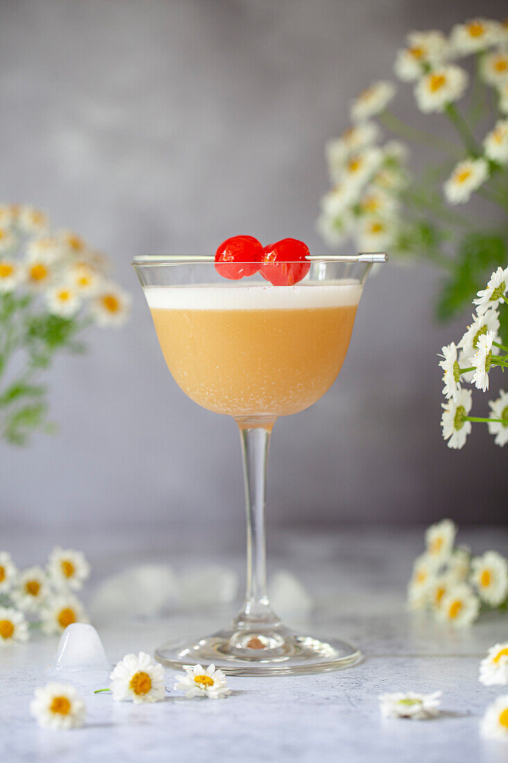 An Amaretto sour cocktail garnished with egg white foam and cocktail cherries