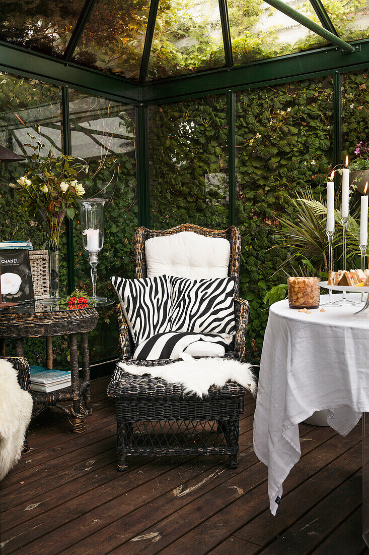 Round table set with tablecloth, armchair with animal-print cushion and footstool in conservatory