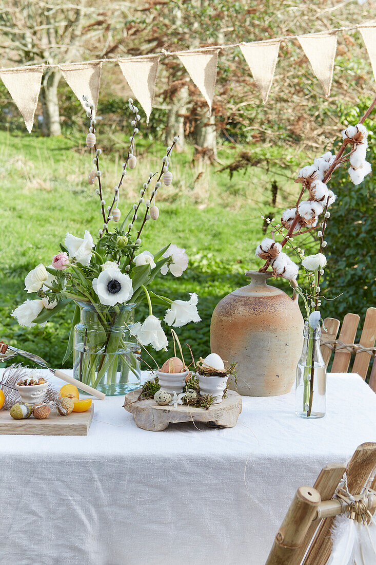 Table set for Easter meal outdoors with white flowers and cotton boll stems below string of bunting