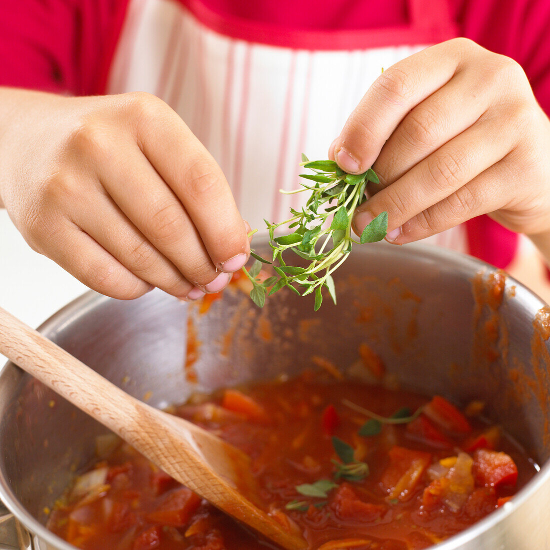 Boy adding thyme leaves to tomato soup mixture
