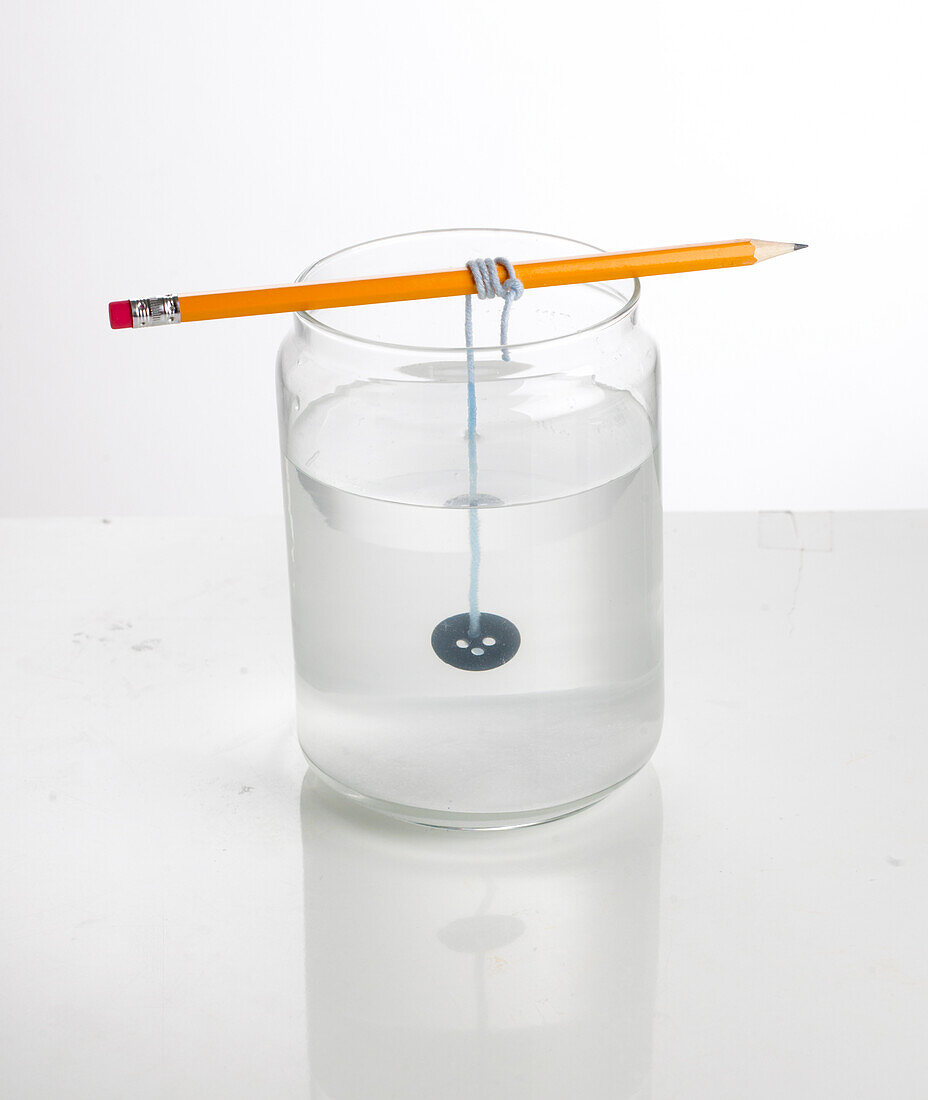 Button tied to pencil and hanging in glass of water