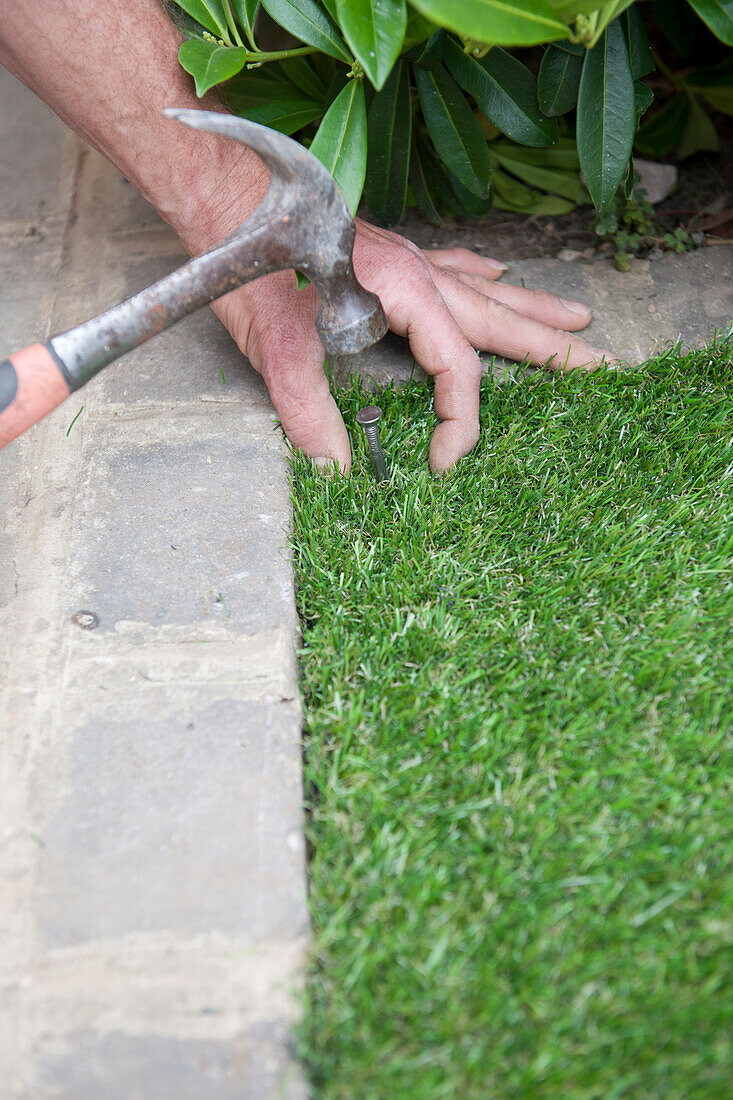 Nailing a sheet of artificial turf in place in one corner