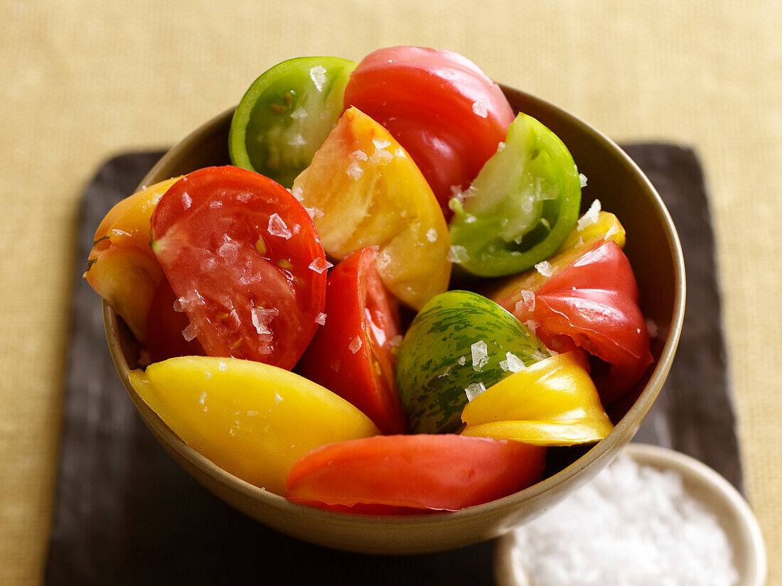 Bowl of various types of tomatoes, chopped, small bowl of salt