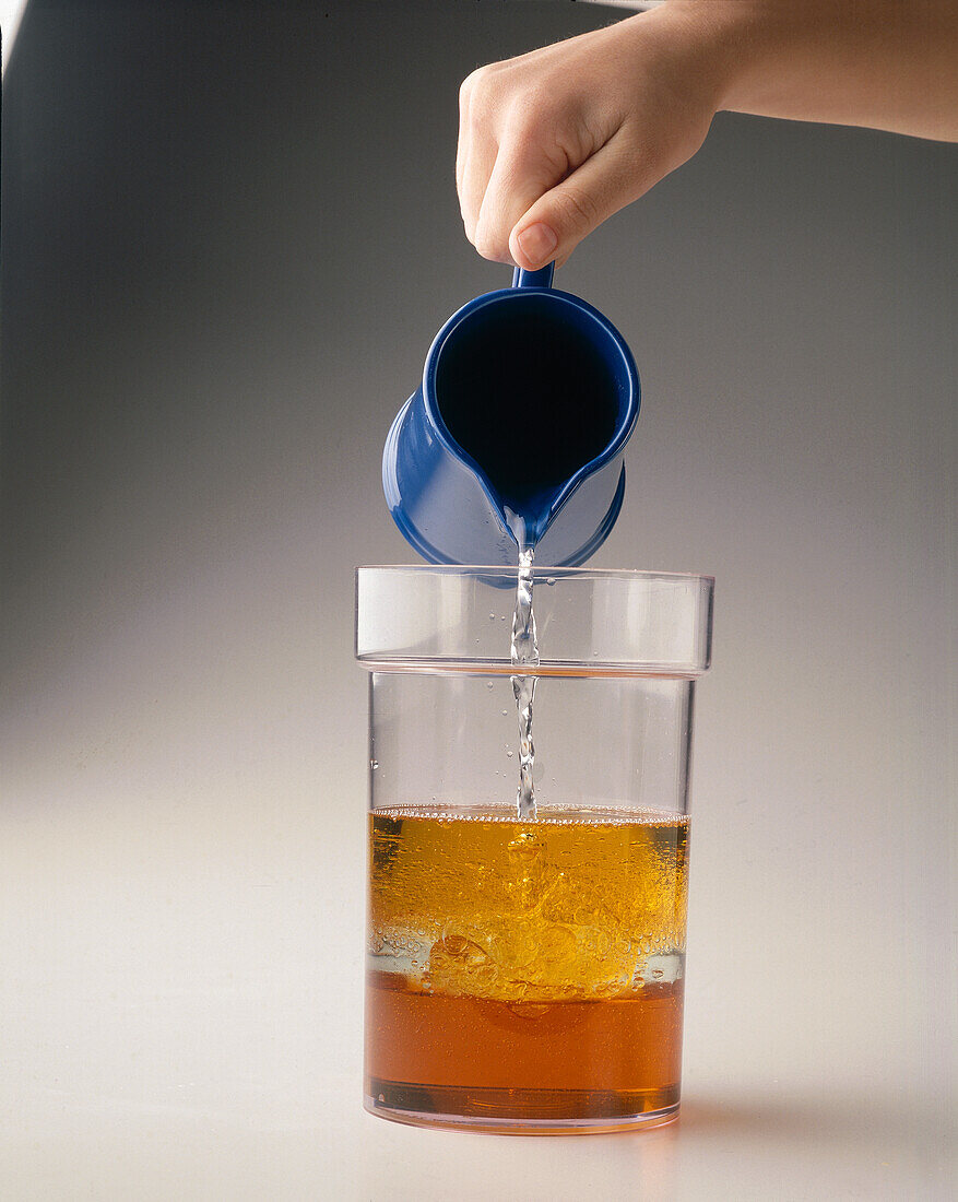 Hand pouring a jug of water into container of oil and syrup