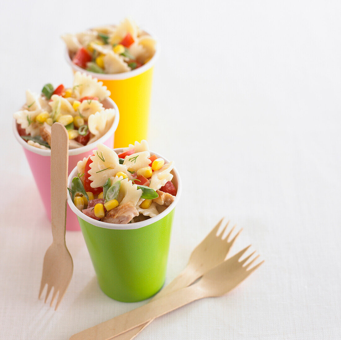 Three brightly coloured cups of pasta salad with forks