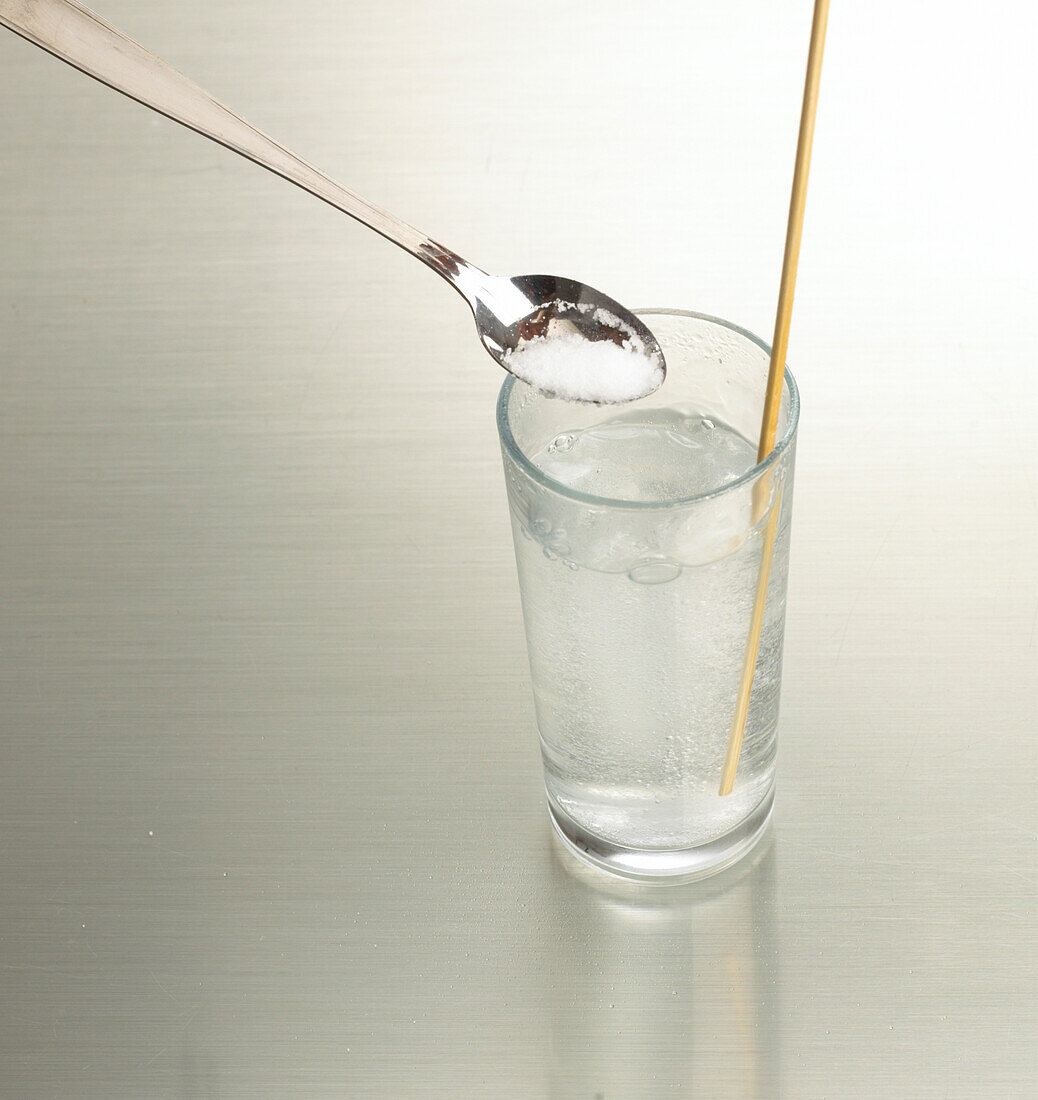 Spoon of salt above glass of carbonated water