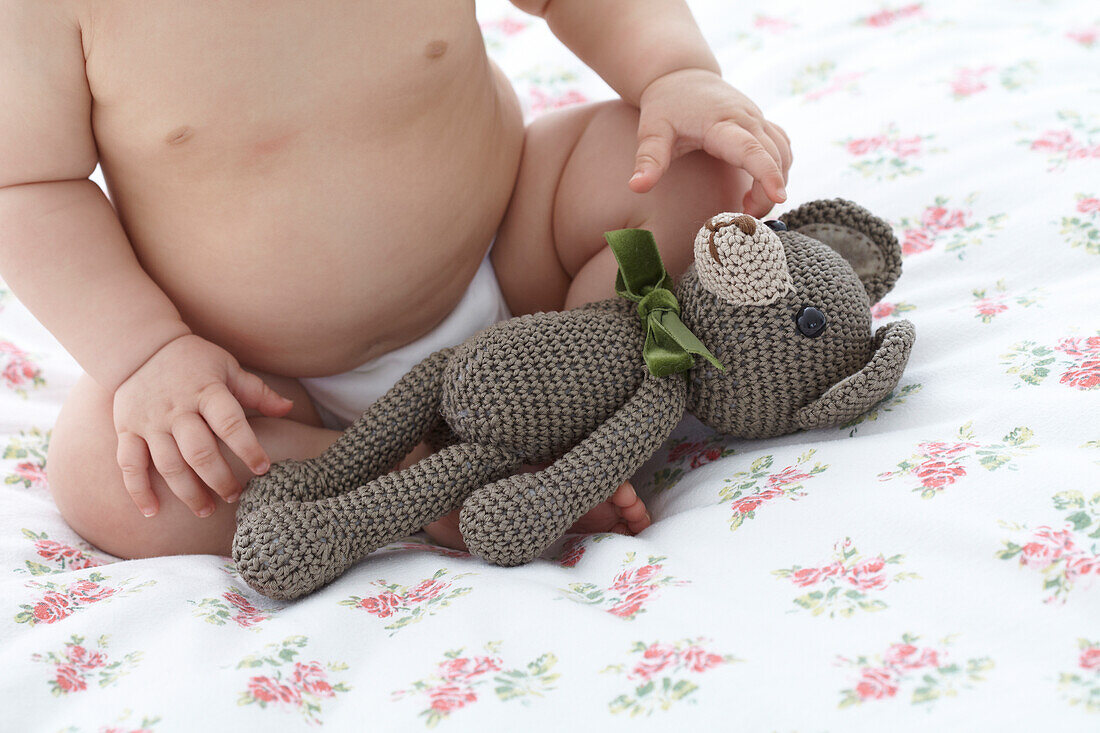 Baby on bed next to crocheted soft toy