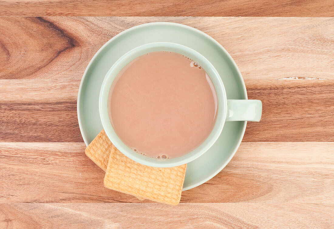 Cup of milky tea with two biscuits on saucer