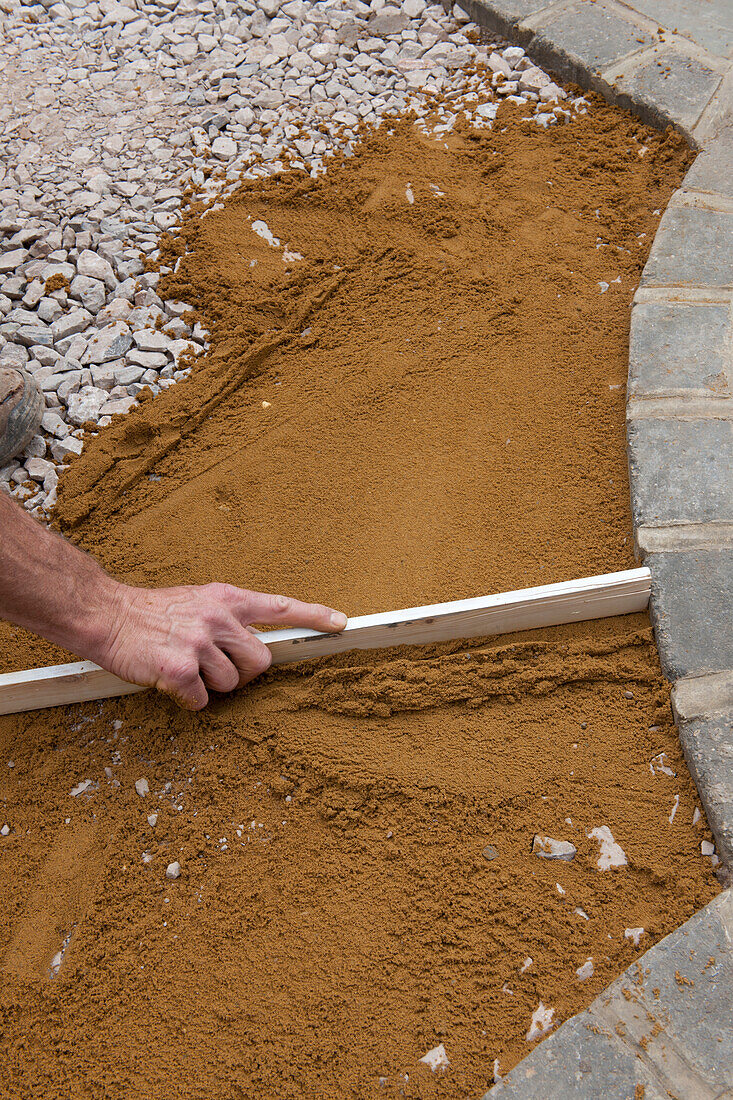 Levelling sand over grit and soil using a piece of wood