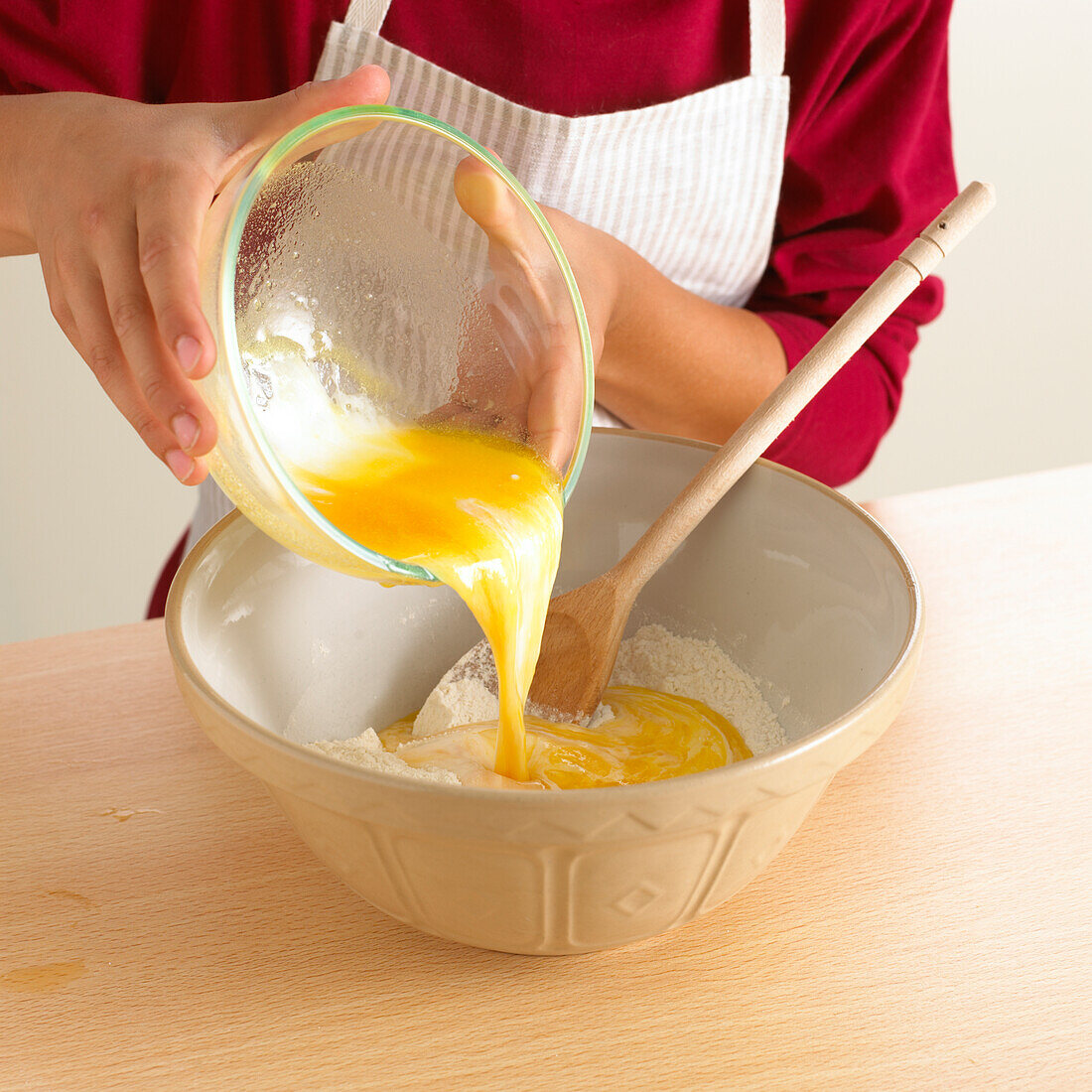 Boy pouring egg yoke from glass bowl into large mixing bowl