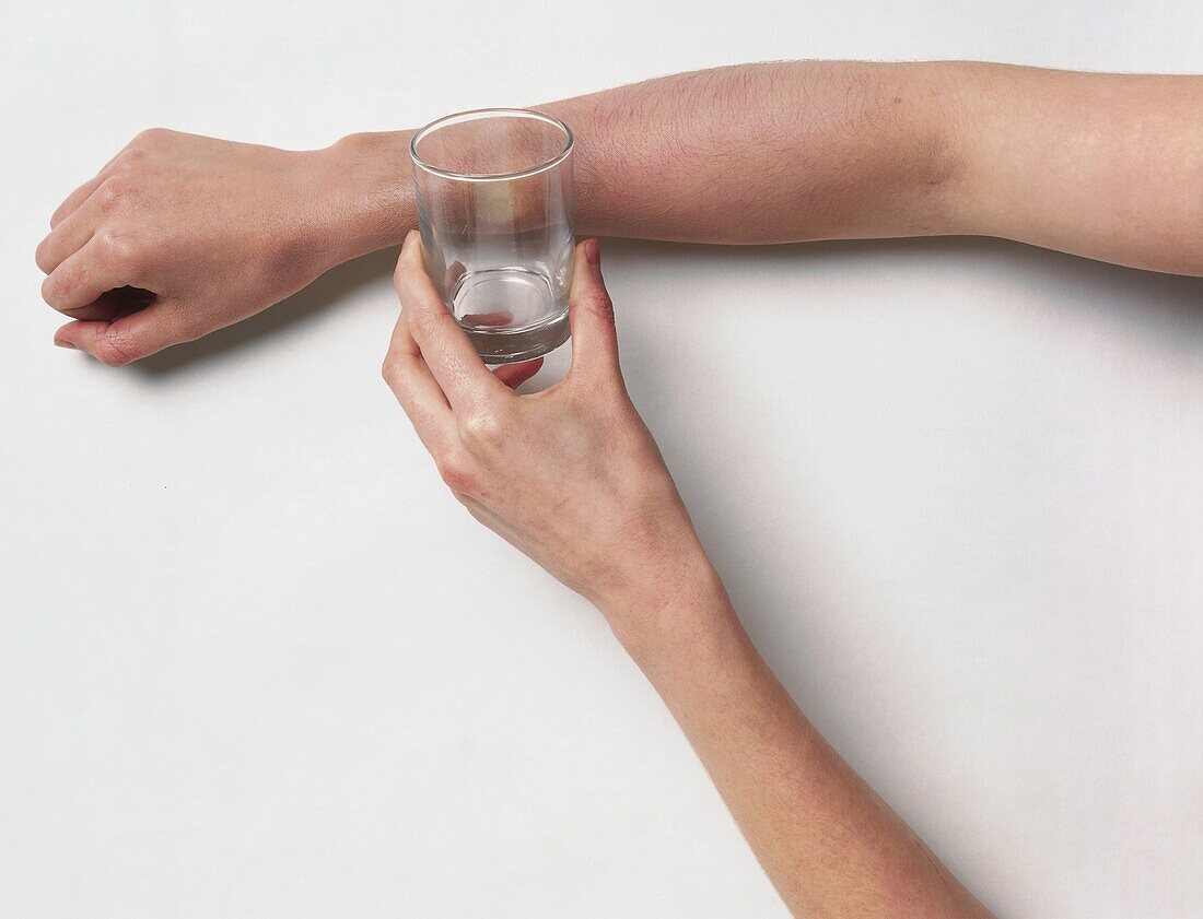 Person placing drinking glass next to their lower arm