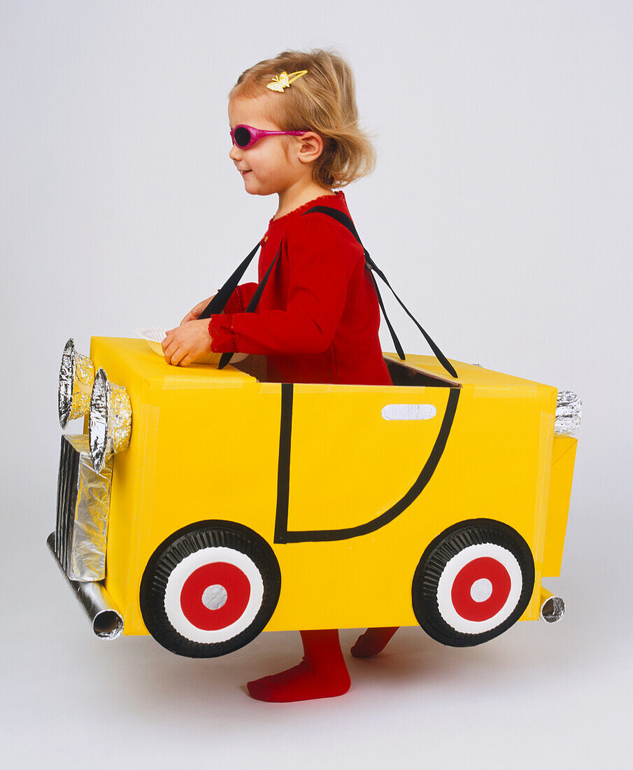 Little girl standing in yellow cardboard car