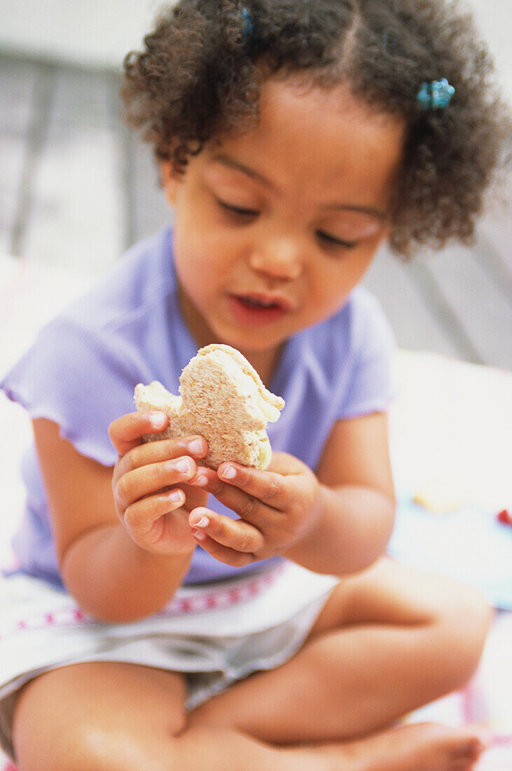 Little girl sat eating a bird shaped sandwich