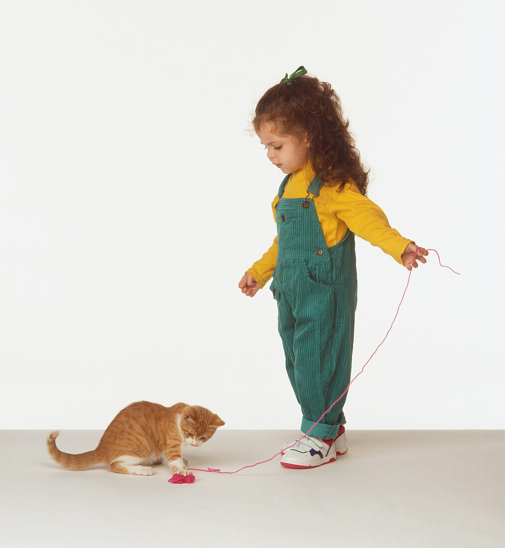 Girl and kitten playing with ball of wool