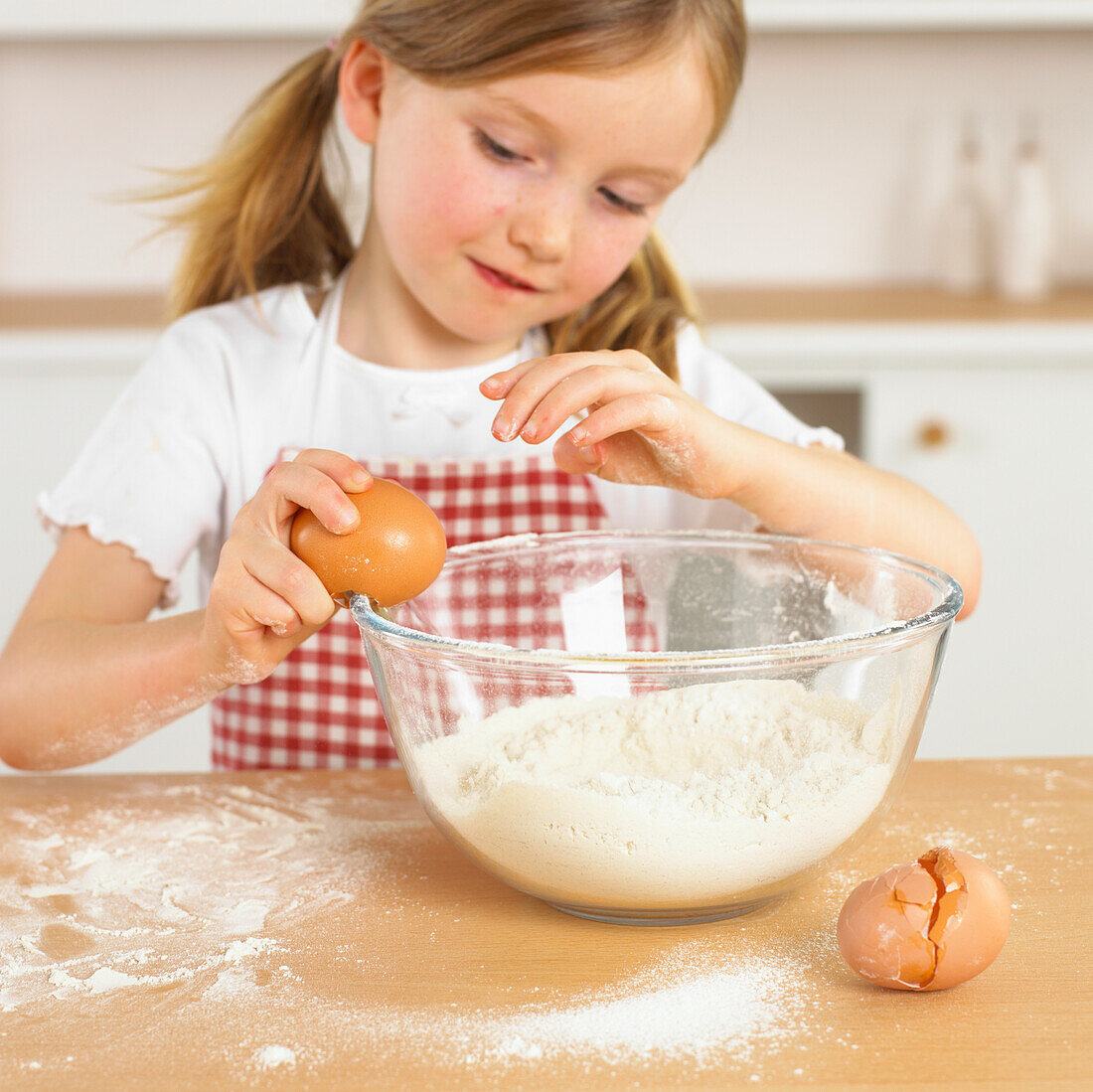 Girl cracking an egg on the side of a bowl of flour