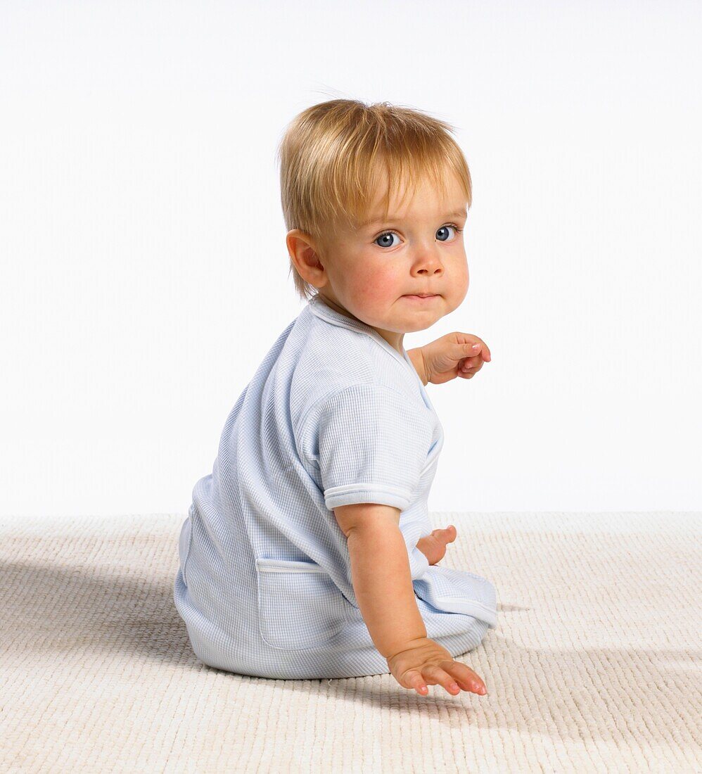 Baby boy in blue pyjamas sitting on floor