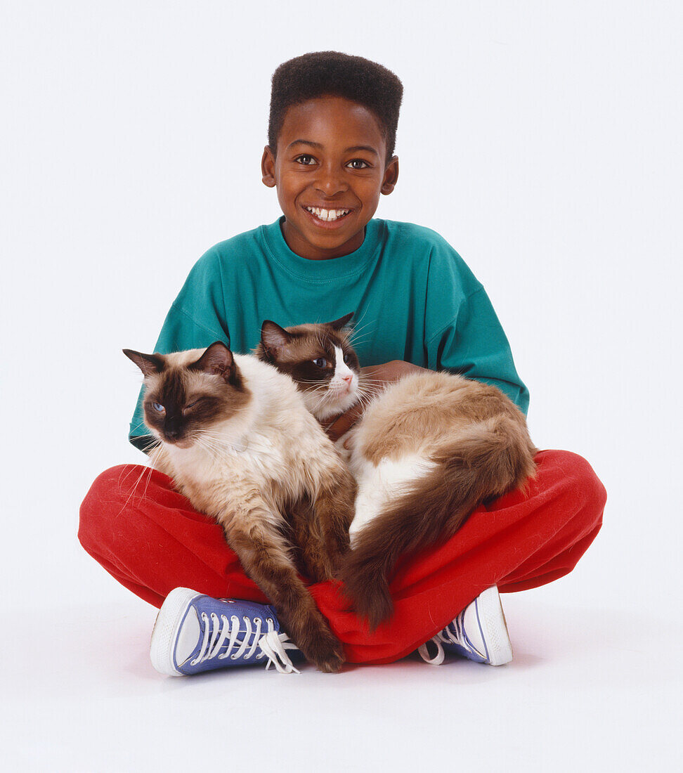 Smiling boy sitting cross-legged on the floor with two cats