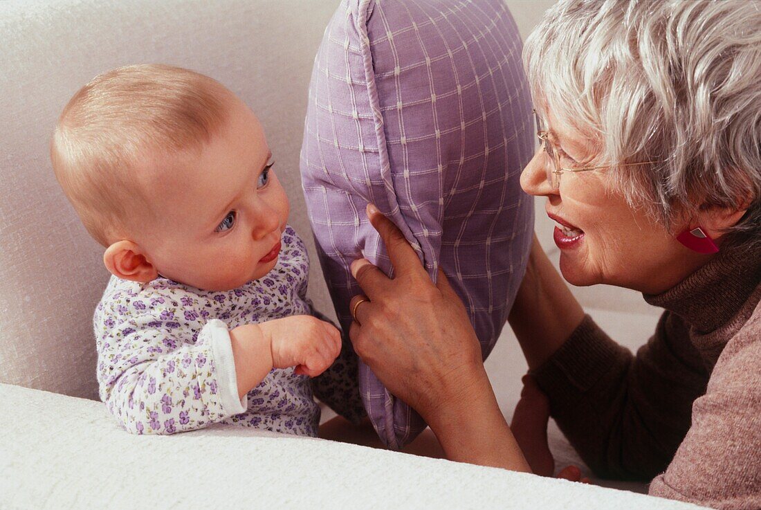 Older woman playing peekaboo with a baby using a cushion