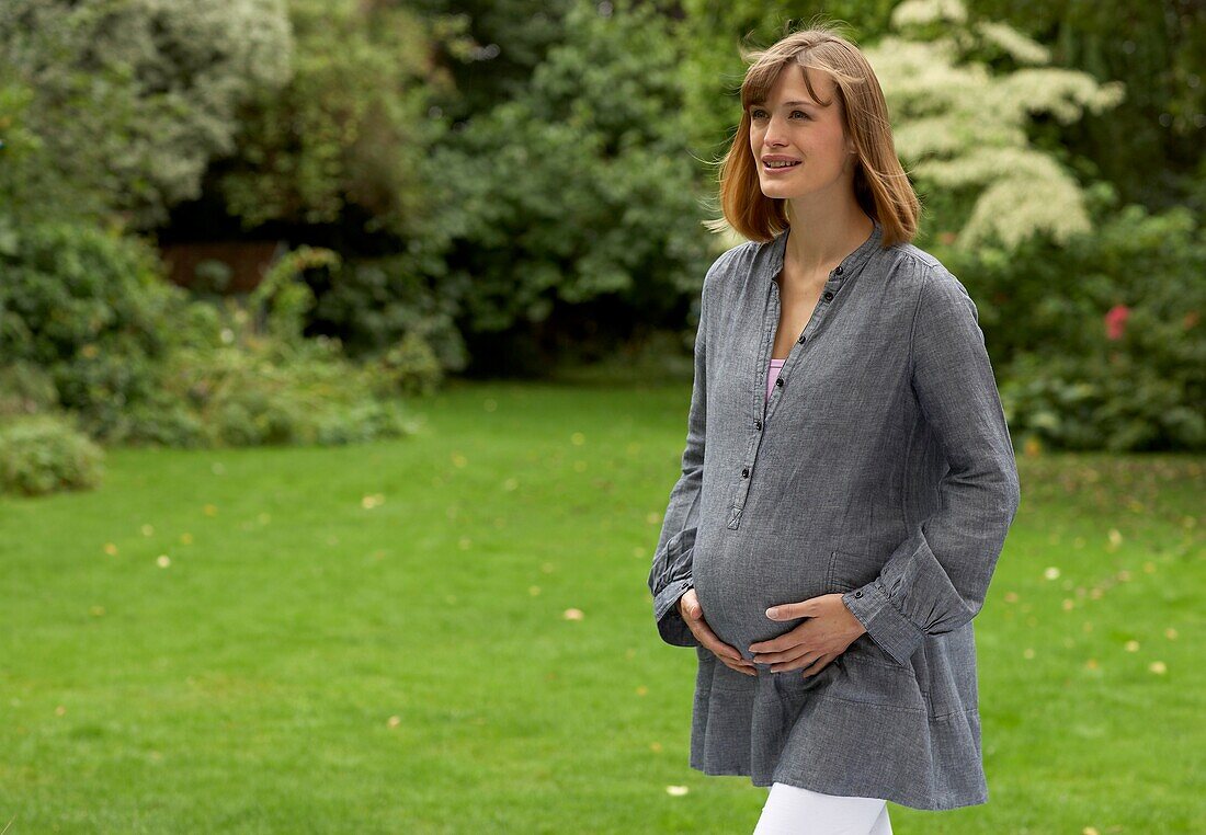 Pregnant woman walking in garden, her hands on her belly