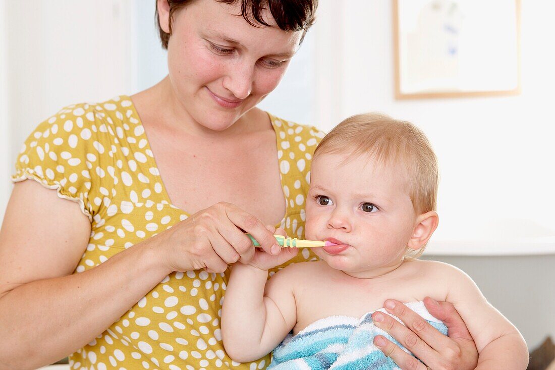 Woman helping baby boy clean his teeth