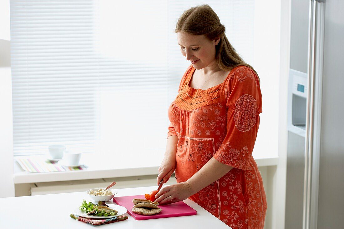 Pregnant woman making midday meal in kitchen