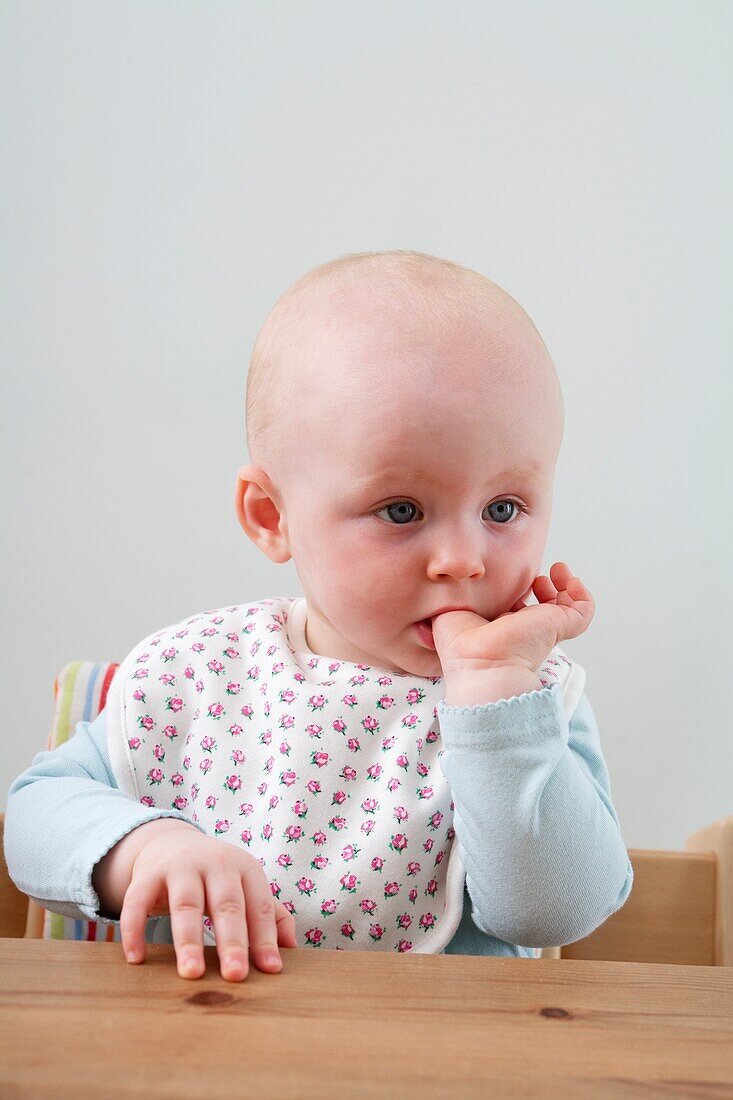 Baby girl sitting at table with a finger in her mouth