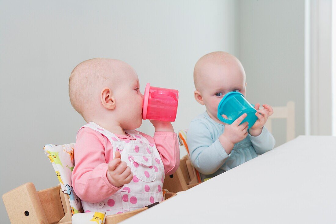 Twin baby girls seated at a table drinking from plastic cups