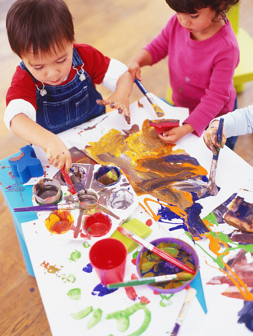 Three children around a table, dipping brushes in paint