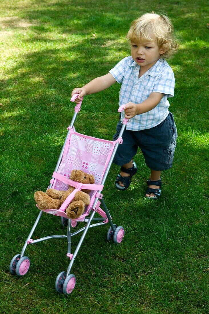 Blonde baby boy with toy pushchair in garden