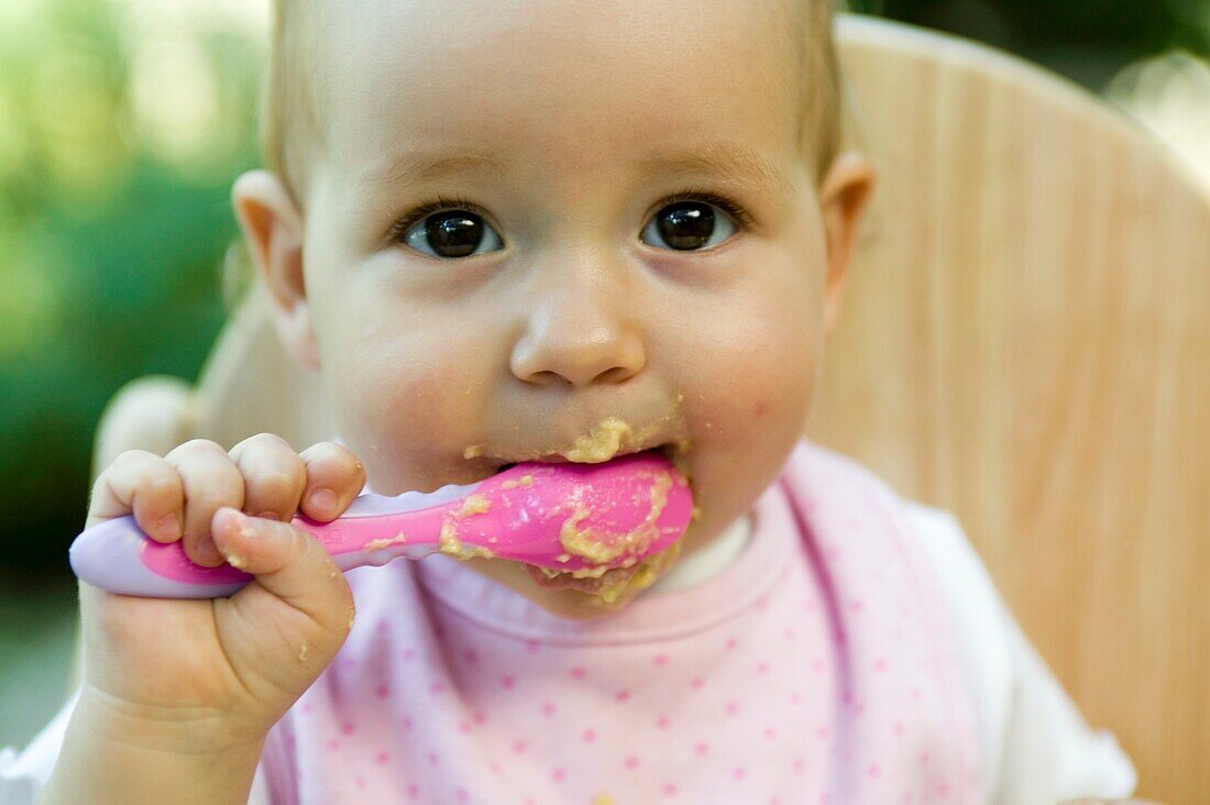 Baby girl holding spoon of baby food to her mouth