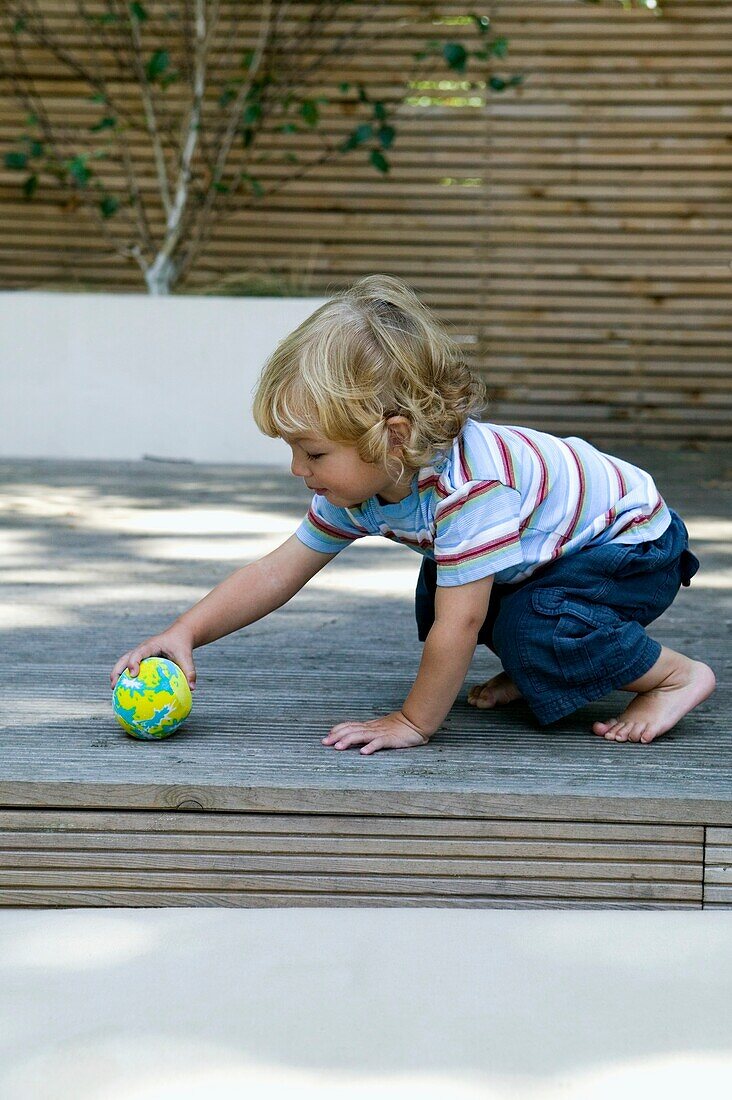 Blonde toddler picking up ball on patio