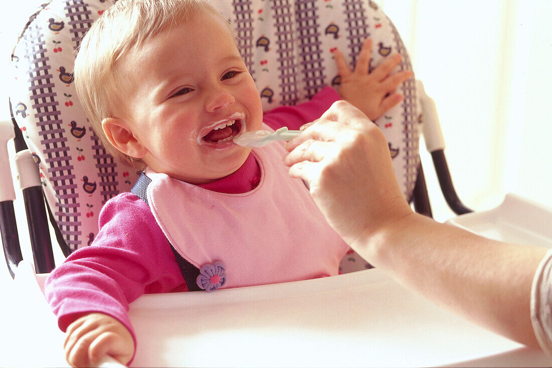 Baby being fed in a high chair, smiling, laughing
