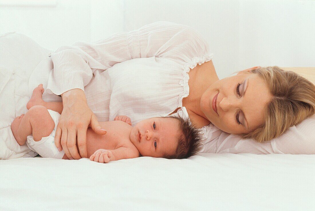 Woman lying beside a baby boy with her hand on his stomach