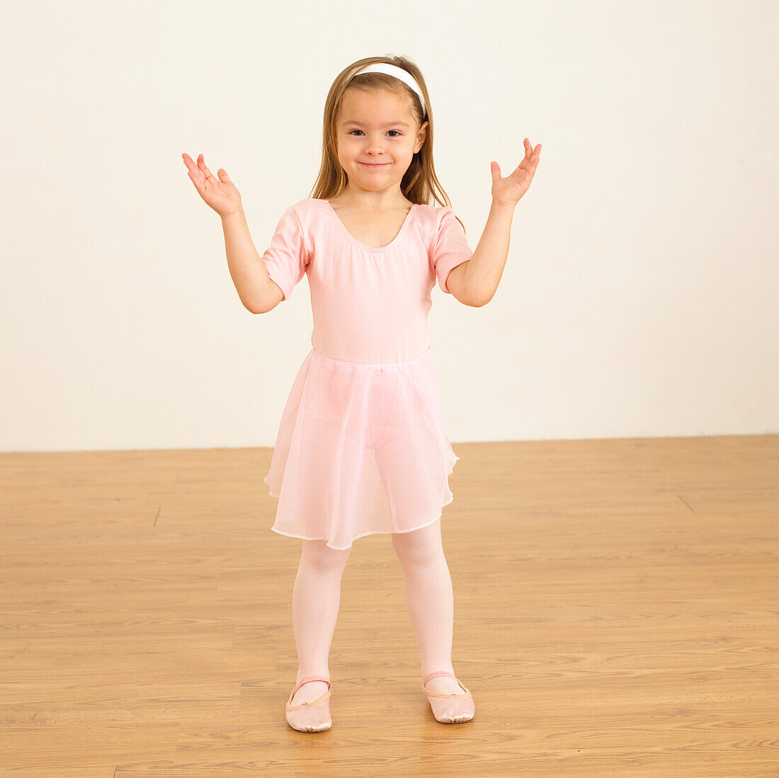 Girl in ballerina outfit standing with hands raised