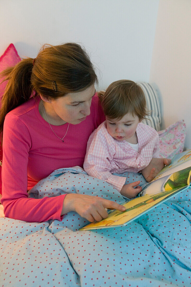 Woman and baby reading a book under a quilt