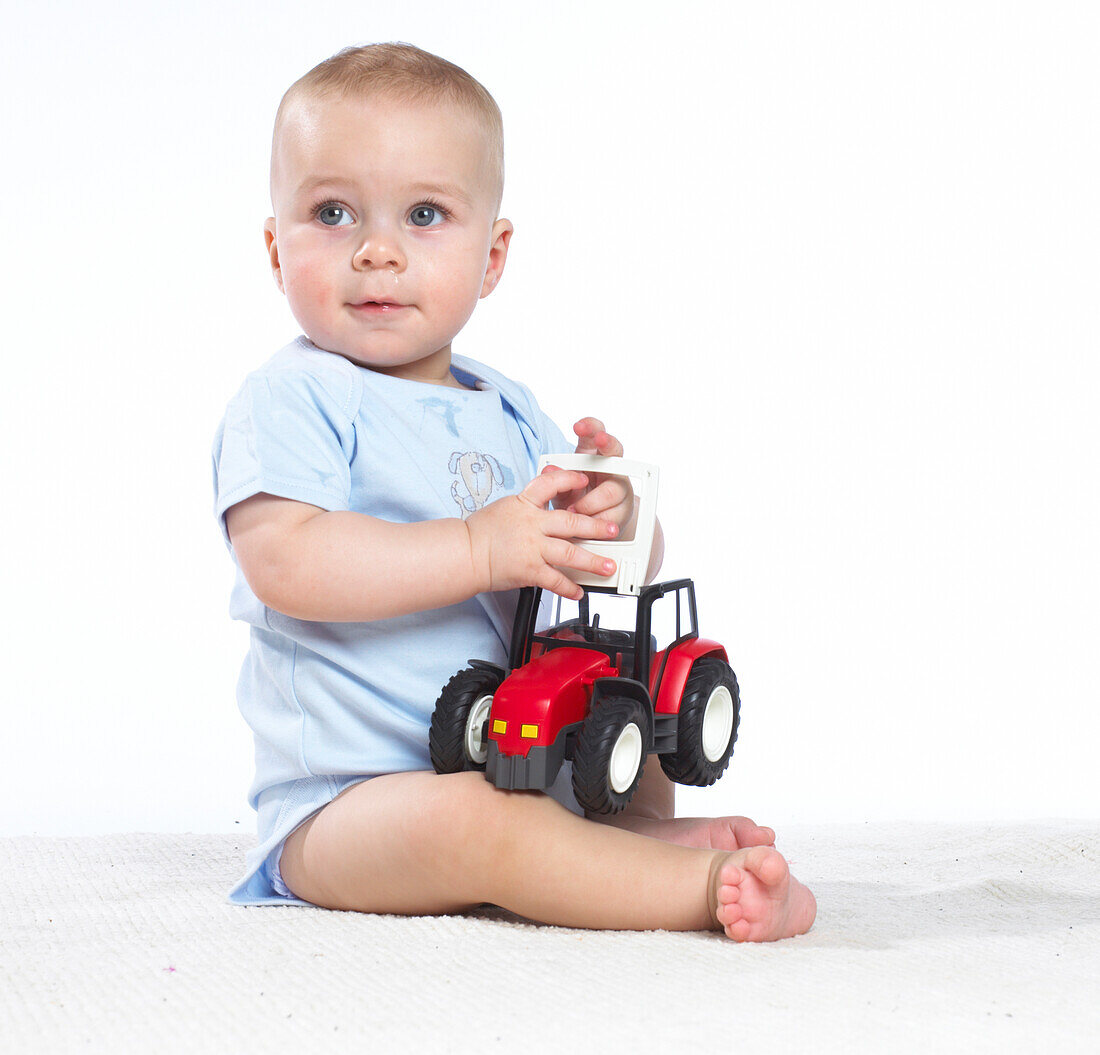 Baby boy sitting on floor playing with toy tractor