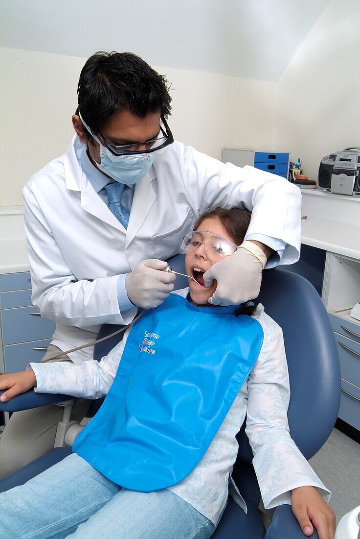 Dentist wearing mask holding drill in girl's mouth