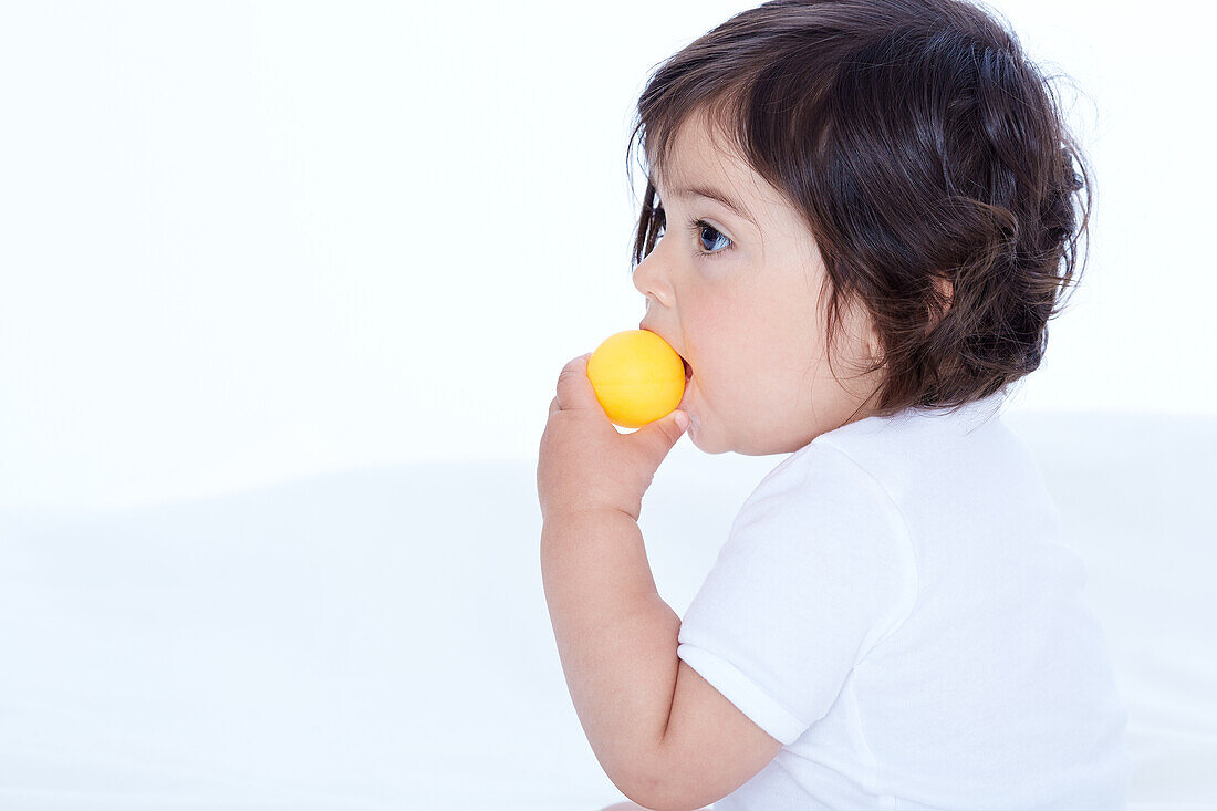 Baby girl biting into yellow ball