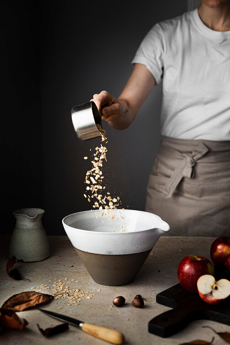 A baker pouring oats into a bowl