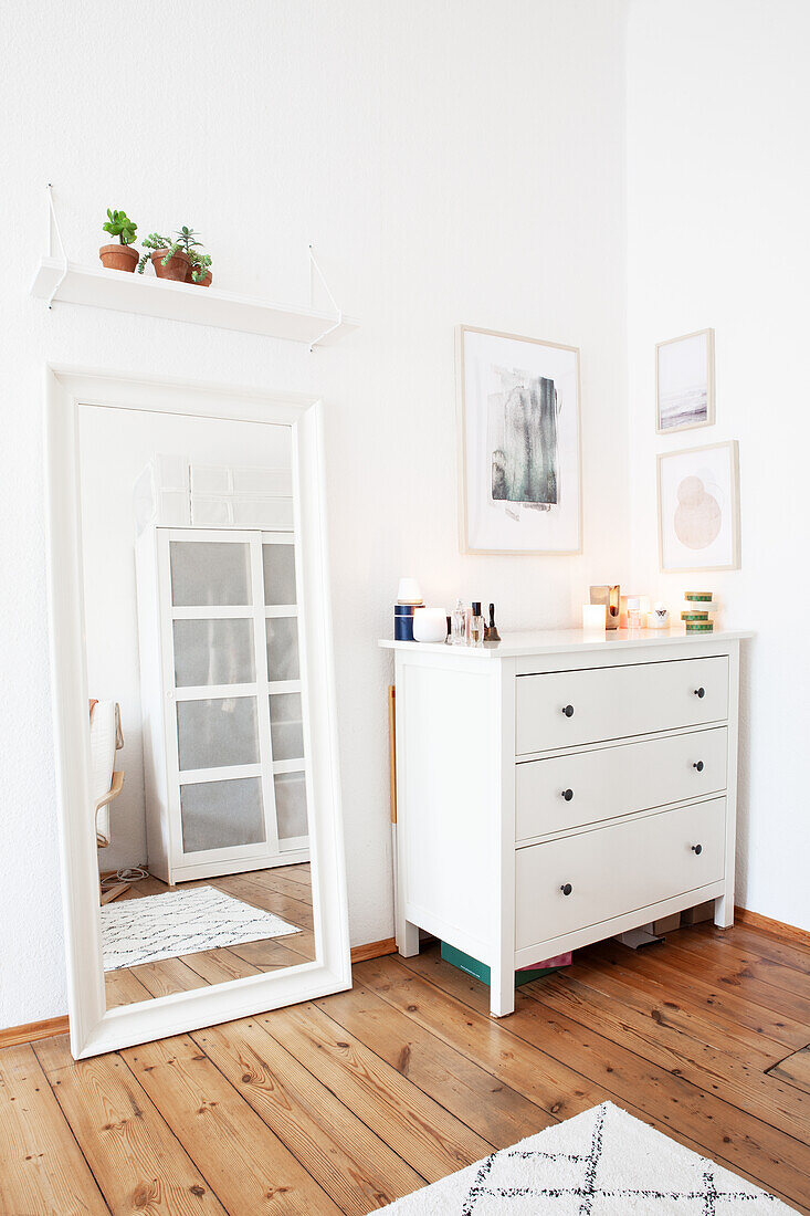 White chest of drawers and mirror on wooden floorboards