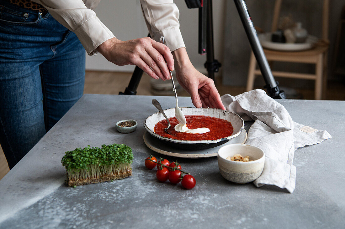 Frauenhände richten Tomatensuppe mit Creme Fraiche an