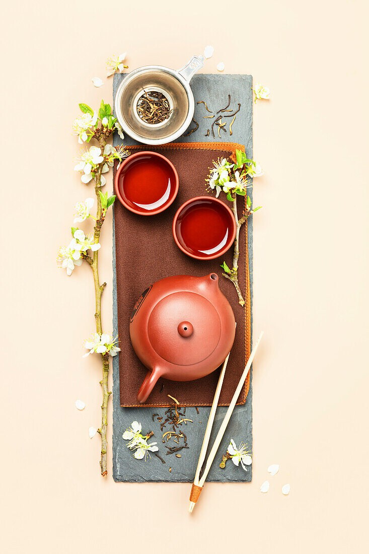 Asian Tea set on stone slate board, ceramic teapot, cups, dried tea and spring branches
