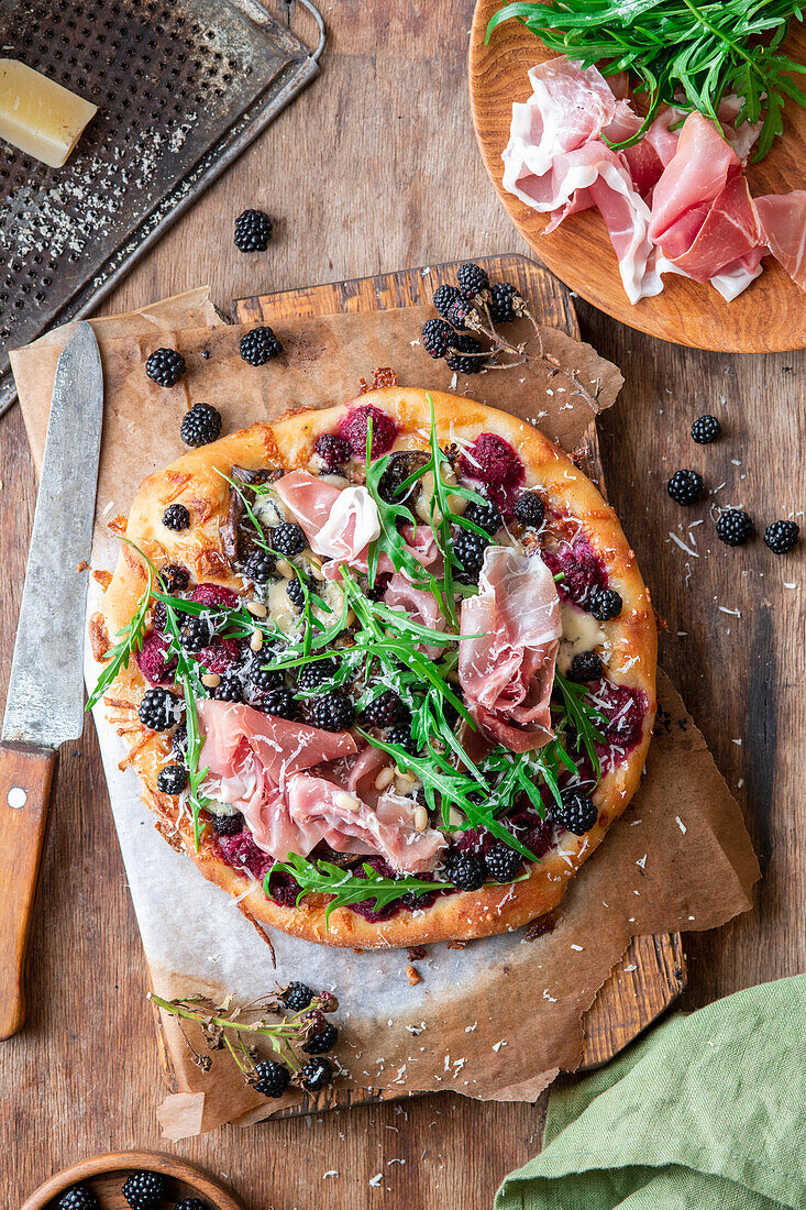 Brombeerpizza mit frischen und gebackenen Beeren, Rucola, Rohschinken und Pinienkernen