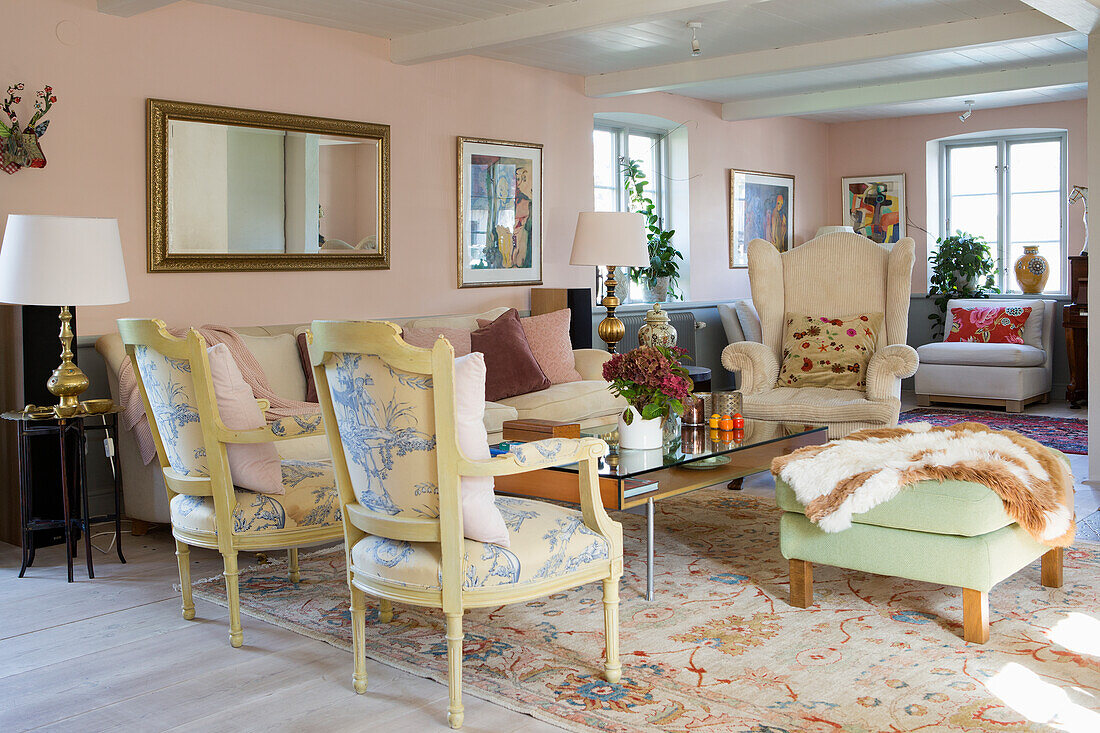 Various pieces of seating furniture in the living room with pale pink walls and white wood-beamed ceiling