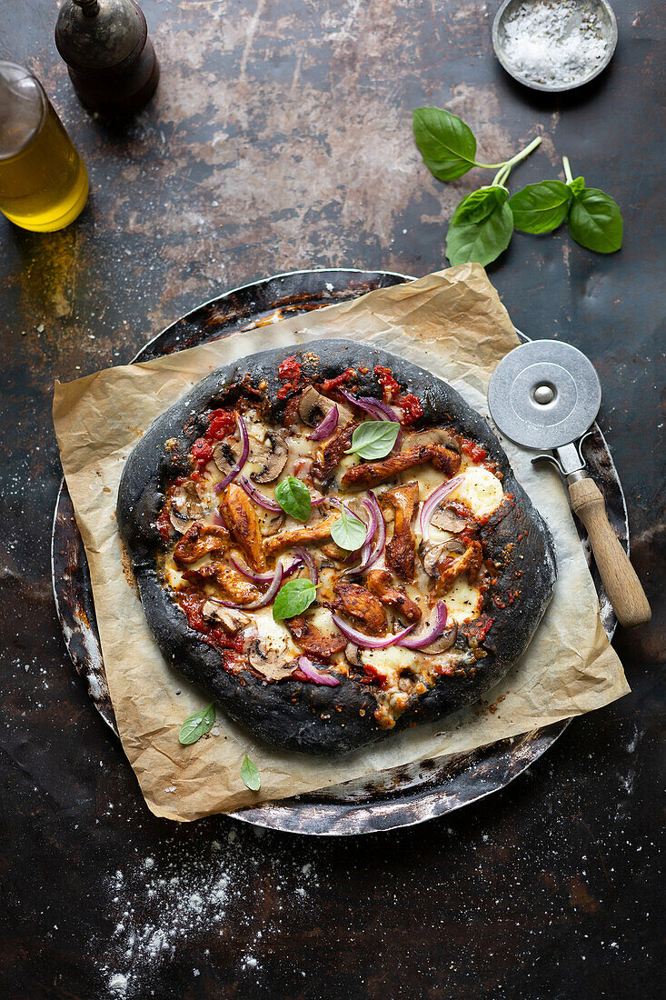 Schwarze Pizza mit Grillhähnchen, Champignons und roten Zwiebeln
