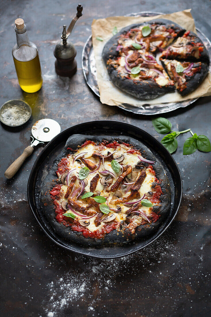 Schwarze Pizza mit Grillhähnchen, Champignons und roten Zwiebeln