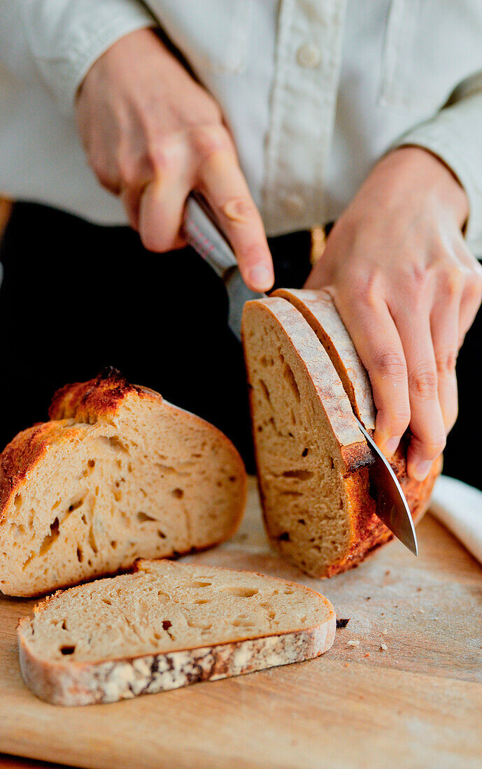 A woman is cutting sourdough bread with a knife