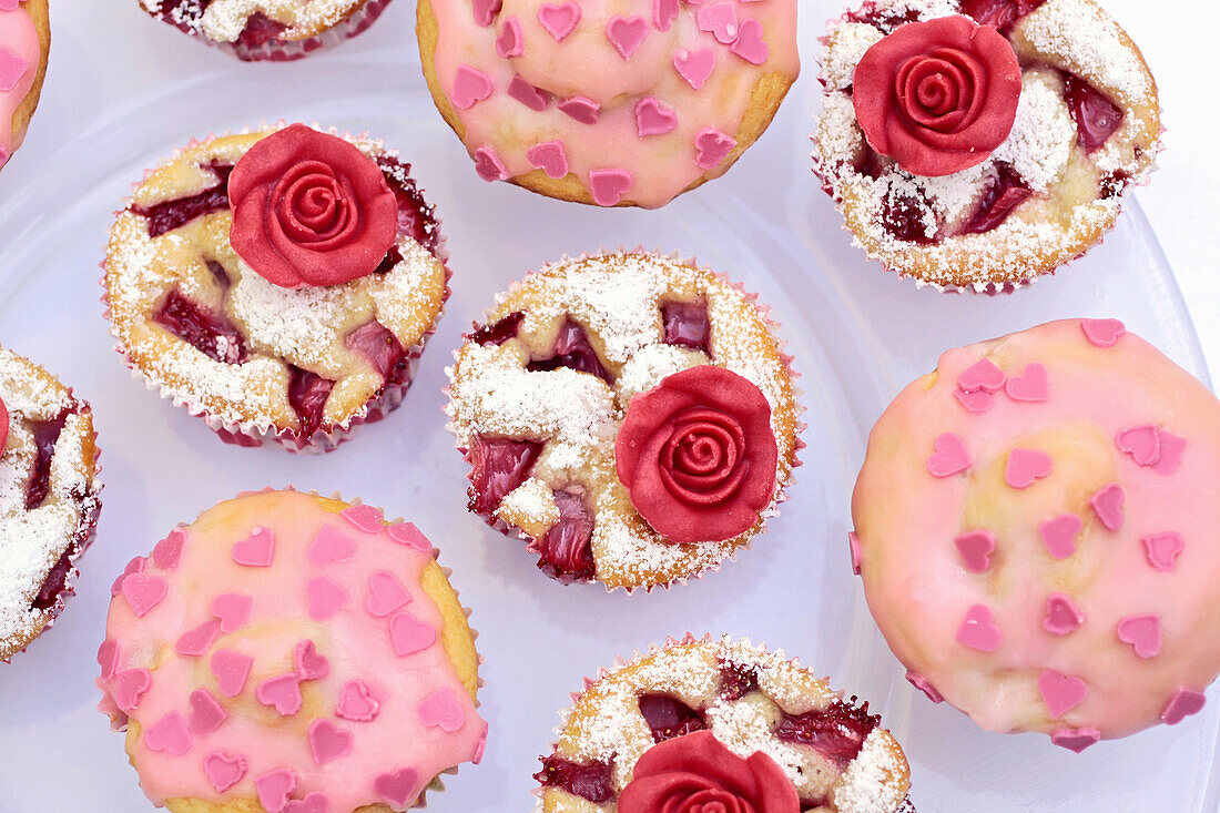 Kirschmuffin mit roter Marzipanrose und Muffins mit rosa Glasur und Zuckerherzen